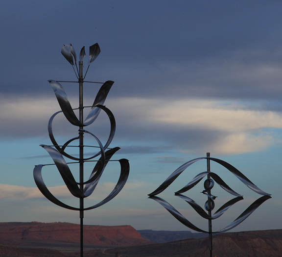 Two metal sculptures of flowers are standing in front of a mountain range. Description generated by AI
