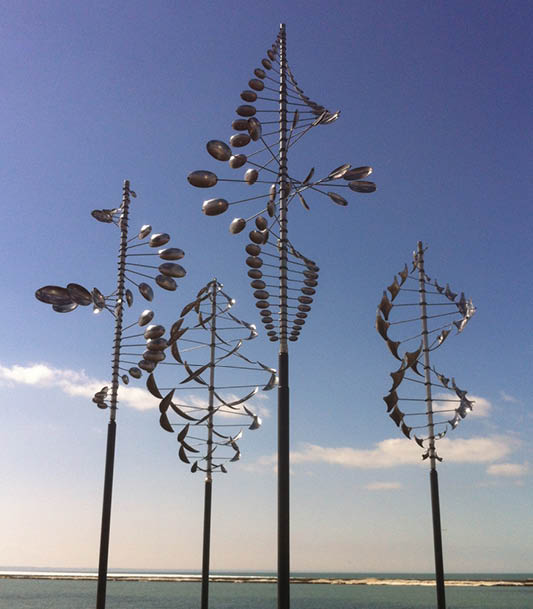 Three metal sculptures of leaves and flowers are standing in a field. Description generated by AI