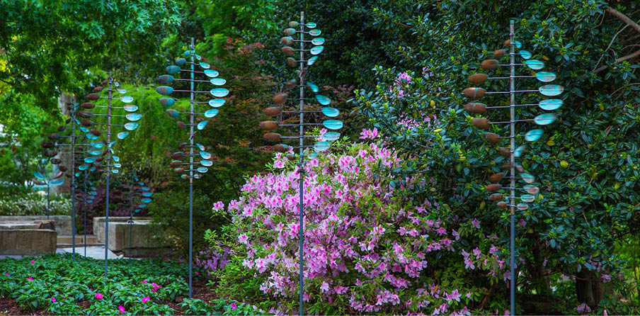 A row of blue and white wind chimes are hanging in front of a flowering bush. AI generated content