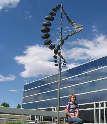 A woman is sitting on a concrete wall in front of a building with a large windmill sculpture. AI generated content